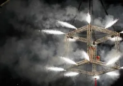 Sabato 27 agosto gli artisti si esibiranno, a luci pubbliche spente,  in un cubo fatto di americane, sospeso su una gru di 80 tonnellate